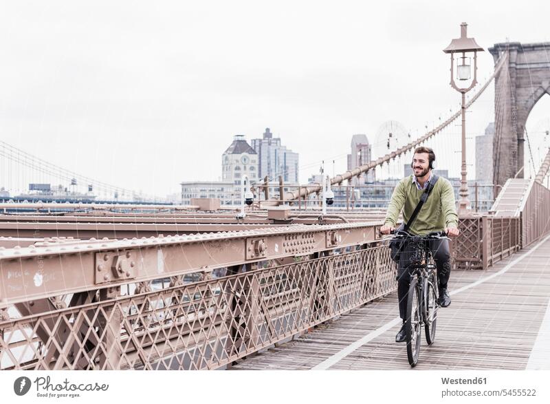USA, New York City, Mann auf dem Fahrrad auf der Brooklyn Bridge New York State Kopfhörer Kopfhoerer lächeln Brücke Bruecken Brücken Bikes Fahrräder Räder Rad