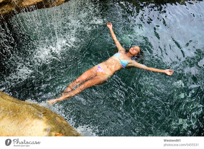 Junge Frau schwimmt im Wasser im Pool mit Wasserfall weiblich Frauen Erwachsener erwachsen Mensch Menschen Leute People Personen Urlaub Ferien Reise Travel