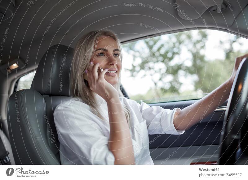 Lächelnde Geschäftsfrau am Handy beim Autofahren fahrend fahrender fahrendes lächeln telefonieren anrufen Anruf telephonieren Mobiltelefon Handies Handys
