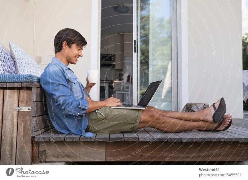Mann sitzt mit Laptop auf der Terrasse Notebook Laptops Notebooks lächeln Terrassen Männer männlich sitzen sitzend Computer Rechner Erwachsener erwachsen Mensch