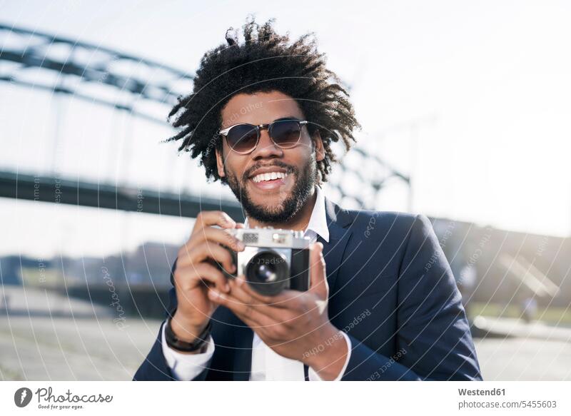 Lächelnder Mann im Anzug am Flussufer mit einer Oldtimer-Kamera Männer männlich Fotoapparat Fotokamera lächeln Erwachsener erwachsen Mensch Menschen Leute