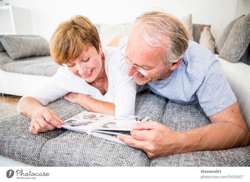 Älteres Ehepaar zu Hause auf dem Sofa liegend und Fotoalbum anschauend Fotoalben Couches Liege Sofas lächeln entspannt entspanntheit relaxt Paar Pärchen Paare