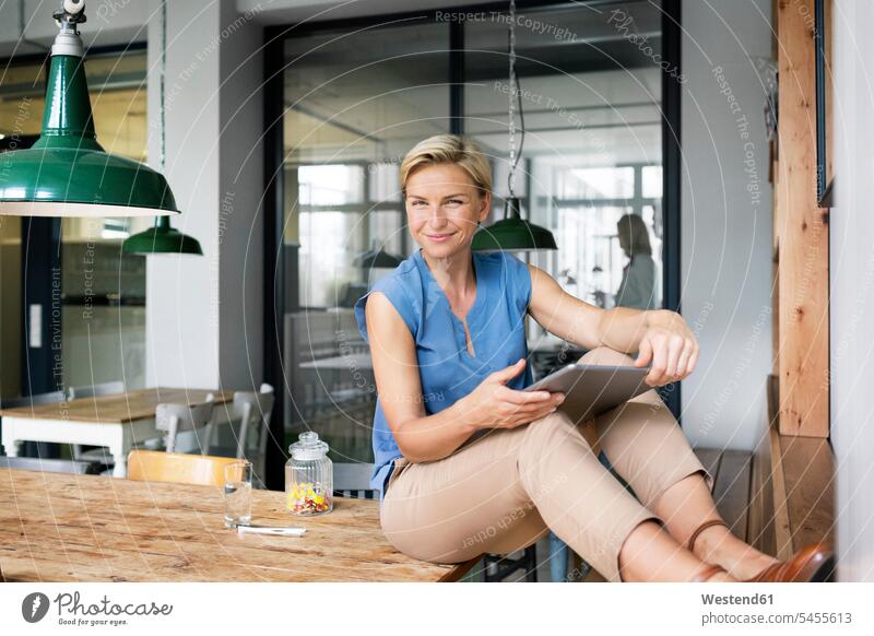 Porträt einer lächelnden blonden Frau mit Tablette auf dem Tisch sitzend weiblich Frauen Tablet Computer Tablet-PC Tablet PC iPad Tablet-Computer Geschäftsfrau