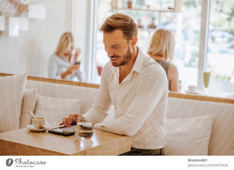 Mann benutzt Tablette in einem Cafe mit zwei Frauen im Hintergrund Geschäftsmann Businessmann Businessmänner Geschäftsmänner Männer männlich Tablet Computer