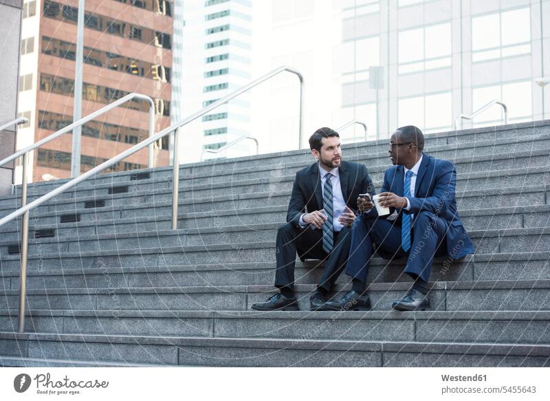 Zwei Geschäftsleute sitzen auf einer Treppe und unterhalten sich Kollegen Arbeitskollegen Treppenaufgang Geschäftsmann Businessmann Businessmänner