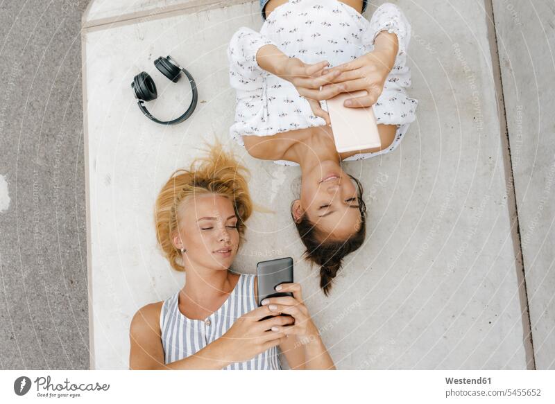 Zwei junge Frauen mit Mobiltelefonen liegen auf einer Rampe in einem Skatepark Freundinnen Handy Handies Handys liegend liegt Auffahrt weiblich Skateboardpark