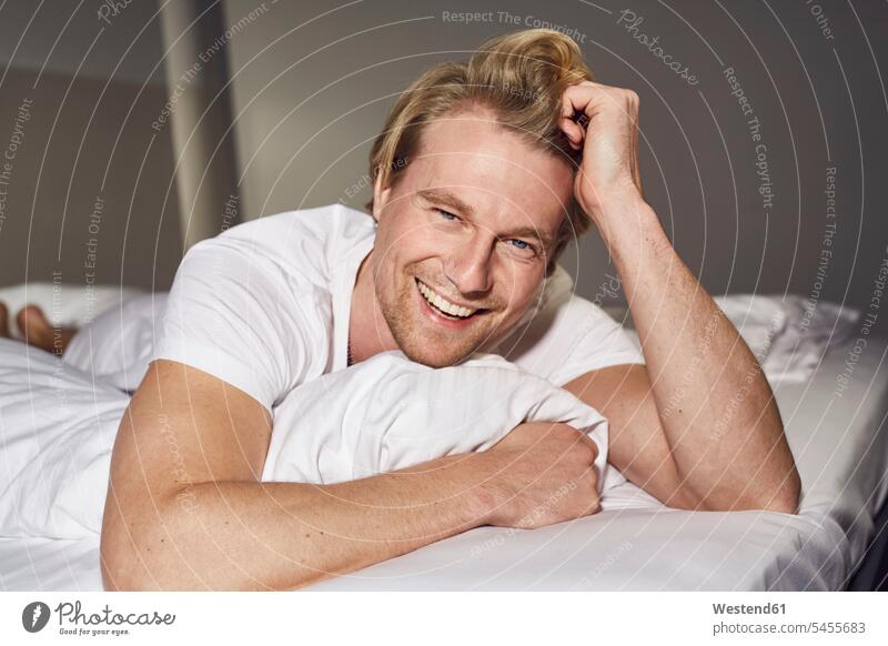Porträt eines lachenden, auf dem Bett liegenden jungen Mannes Portrait Porträts Portraits Betten Männer männlich Erwachsener erwachsen Mensch Menschen Leute