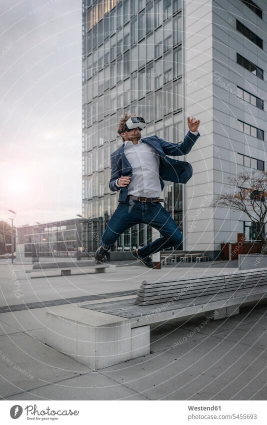 Geschäftsmann mit VR-Brille springt in der Stadt Brillen Businessmann Businessmänner Geschäftsmänner springen hüpfen Virtuelle Realität Virtuelle Realitaet