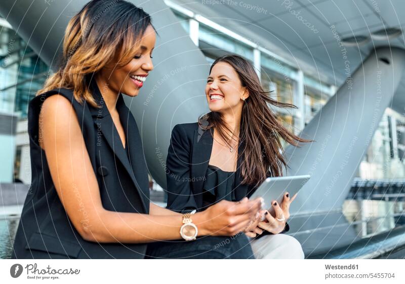 Zwei glückliche Geschäftsfrauen mit einer Tablette in der Stadt Kollegin Kolleginnen Businesswomen Businessfrauen Businesswoman Frau weiblich Frauen lächeln