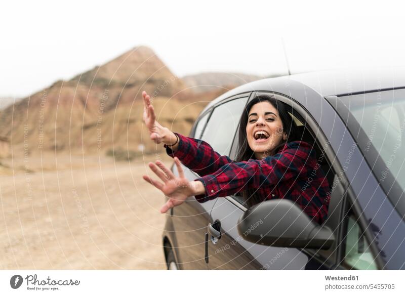 Spanien, Navarra, Bardenas Reales, schreiende und winkende junge Frau, die sich aus dem Autofenster lehnt weiblich Frauen Wagen PKWs Automobil Autos Erwachsener