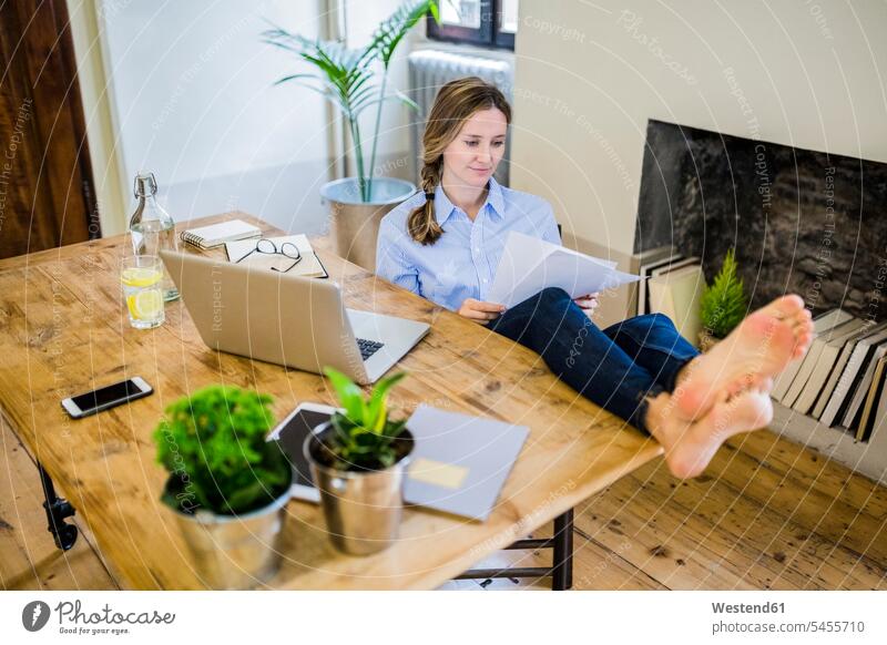 Frau sitzt zu Hause mit den Füßen am Schreibtisch und liest Dokument weiblich Frauen Fuß Fuss lesen Lektüre sitzen sitzend Zuhause daheim Unterlagen