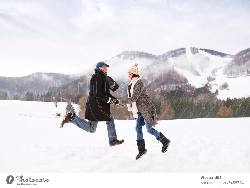 Glückliches älteres Paar springt in schneebedeckter Landschaft in die Luft Seniorenpaar Seniorenpaare ältere Paare Seniorenpärchen Luftsprung Luftsprünge