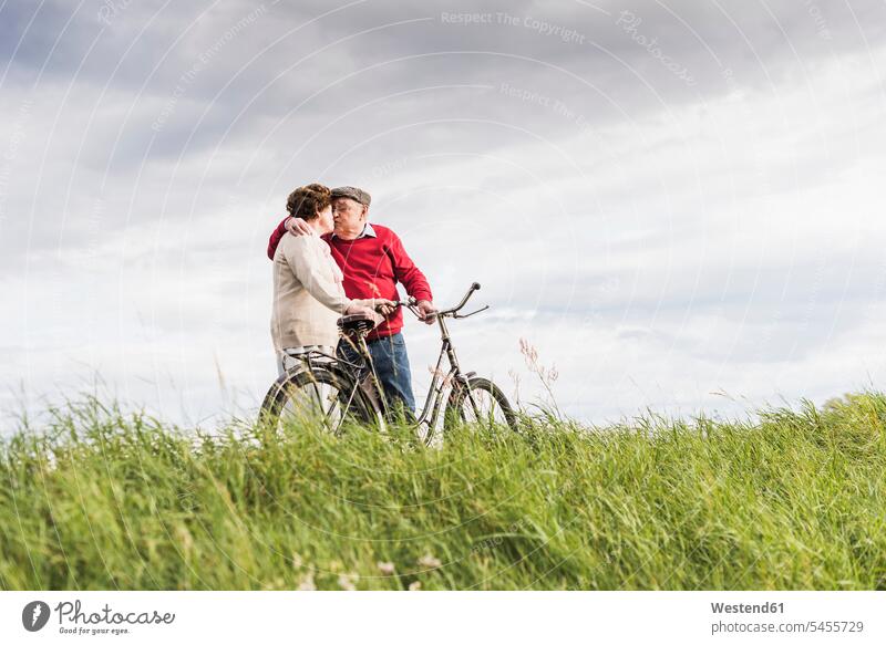 Älteres Ehepaar mit Fahrrädern küsst sich in ländlicher Landschaft Paar Pärchen Paare Partnerschaft Senior ältere Männer älterer Mann Senioren Seniorin