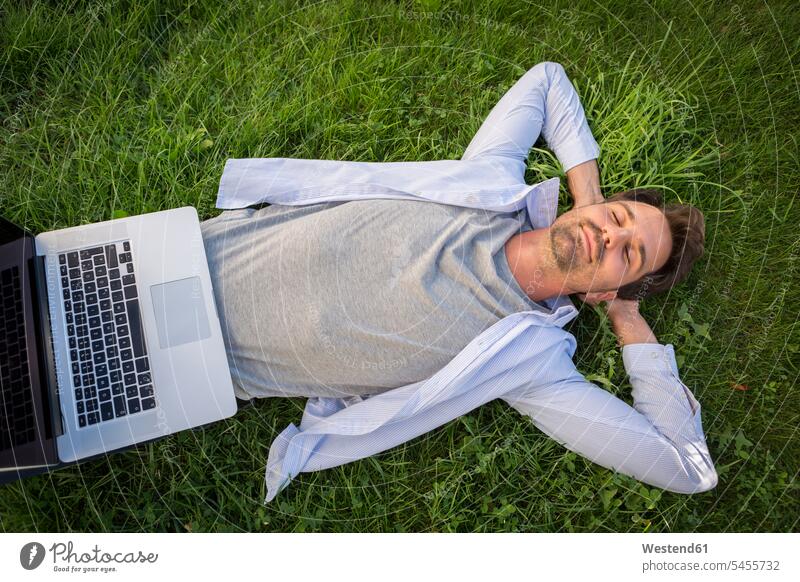 Mann entspannt sich im Sommer auf dem Rasen, mit Laptop auf dem Bauch Notebook Laptops Notebooks Männer männlich tagträumen Tagtraum Entspannung Entspannen