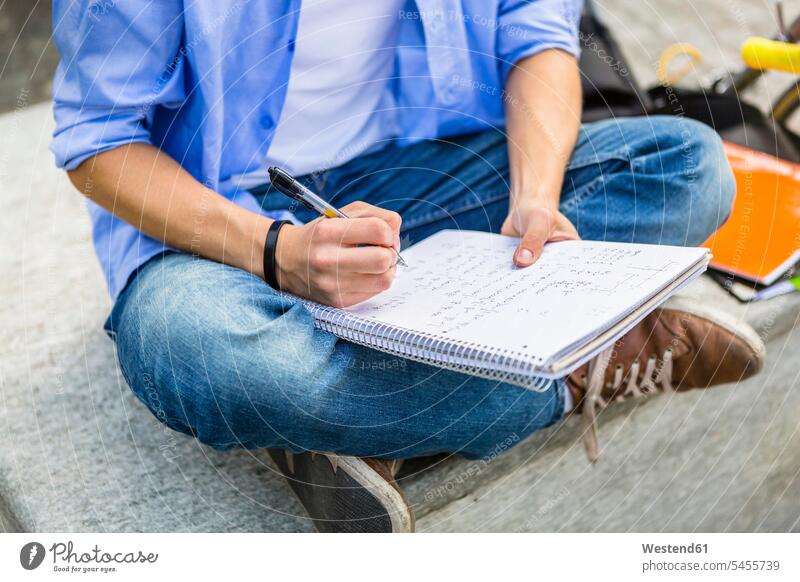 Junger Mann sitzt auf Bank und schreibt auf Notizblock, Teilansicht schreiben aufschreiben notieren schreibend Schrift Student Hochschueler Studierender