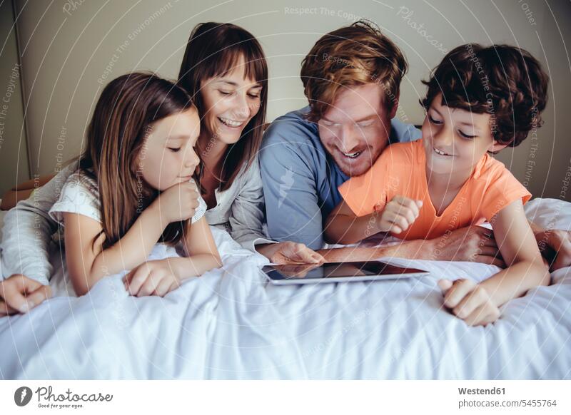 Kinder und ihre Eltern betrachten Tablette auf dem Bett Tablet Computer Tablet-PC Tablet PC iPad Tablet-Computer lachen Familie Familien Betten Rechner positiv
