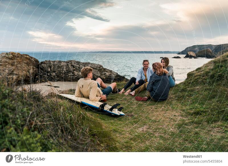 Glückliche Freunde mit Surfbrett beim geselligen Beisammensein an der Küste bei Sonnenuntergang Surfbretter surfboard surfboards Kueste Kuesten Küsten glücklich