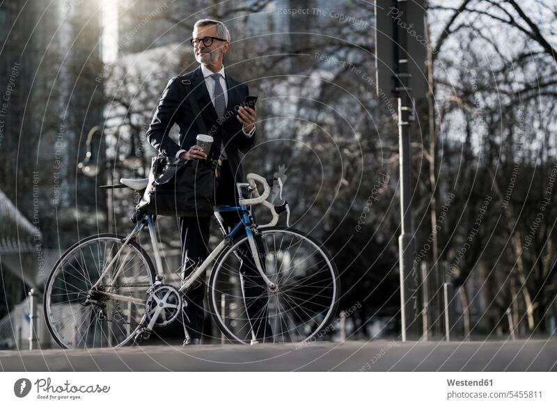 Grauhaariger Geschäftsmann mit Fahrrad und Kaffee zum Mitnehmen in der Stadt Businessmann Businessmänner Geschäftsmänner staedtisch städtisch Bikes Fahrräder