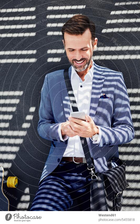 Porträt eines Geschäftsmannes mit Longboard und Telefon in der Nähe einer Betonwand lächeln Handy Mobiltelefon Handies Handys Mobiltelefone stehen stehend steht