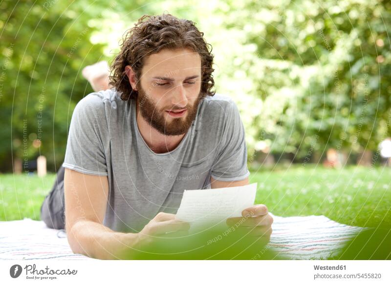 Mann liegt auf einer Decke in einem Park und liest einen Brief Männer männlich Briefe Erwachsener erwachsen Mensch Menschen Leute People Personen Post