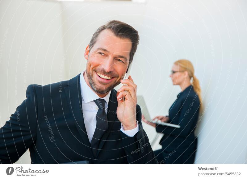 Lächelnder Geschäftsmann am Handy und Geschäftsfrau mit Laptop im Freien Mobiltelefon Handies Handys Mobiltelefone Business Geschäftsleben Geschäftswelt