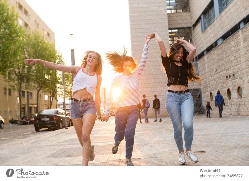 Drei glückliche junge Frauen laufen Hand in Hand auf dem Bürgersteig Freundinnen rennen Freunde Freundschaft Kameradschaft weiblich Erwachsener erwachsen Mensch