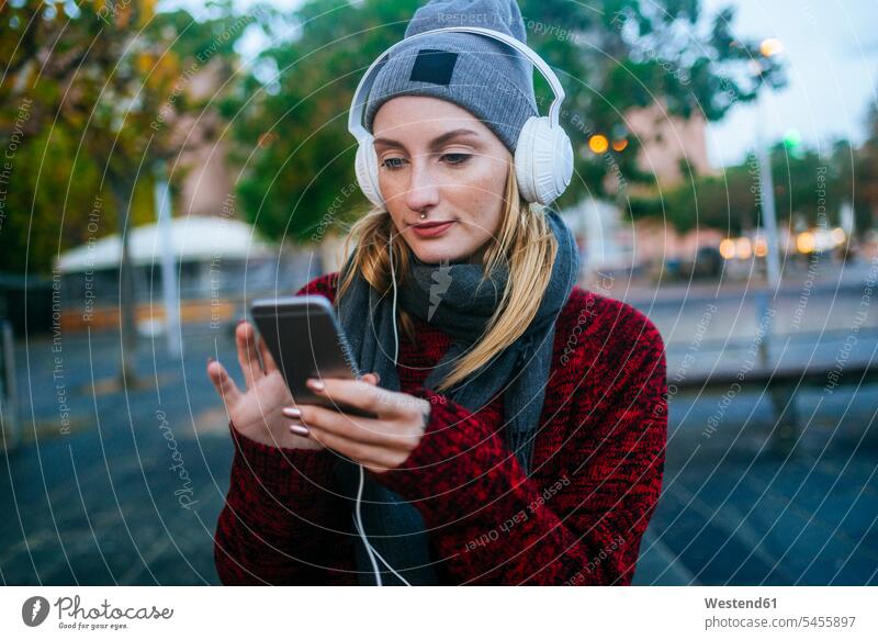 Junge Frau, die mit einem Smartphone Musik hört hören hoeren Kopfhörer Kopfhoerer Handy Mobiltelefon Handies Handys Mobiltelefone weiblich Frauen Telefon