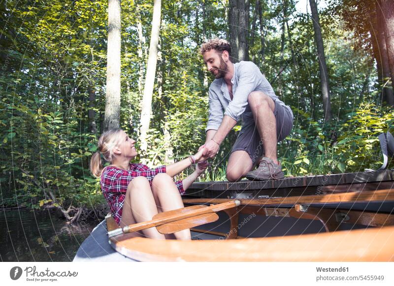Lächelnder junger Mann hilft seiner Freundin in einem Waldbach beim Aussteigen aus dem Kanu Bach Bäche Baeche glücklich Glück glücklich sein glücklichsein Forst