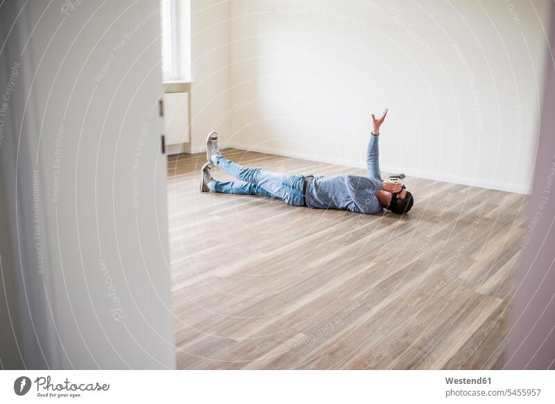Auf dem Boden liegender Mann in leerer Wohnung mit VR-Brille liegt Virtual Reality Brille Virtual-Reality-Brille Virtual Reality-Brille VR Brille wohnen