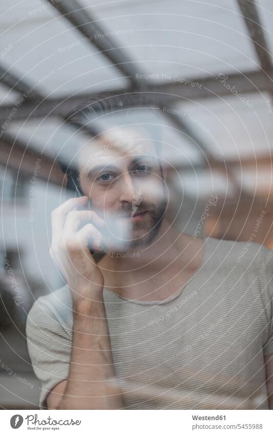 Porträt eines jungen Mannes am Telefon hinter einer Fensterscheibe Männer männlich telefonieren anrufen Anruf telephonieren Erwachsener erwachsen Mensch