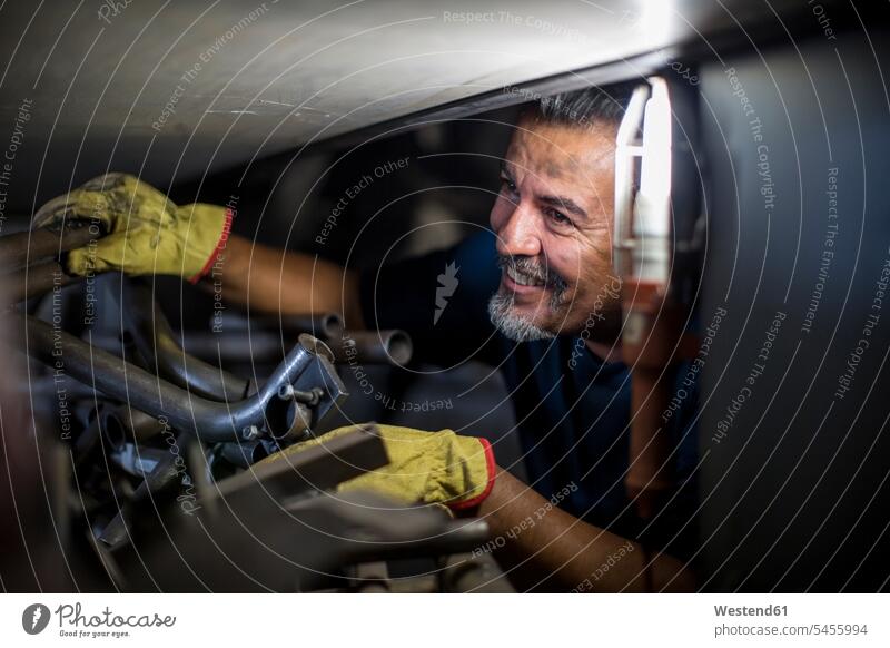 Lächelnder Mechaniker bei der Arbeit am Motorrad in der Werkstatt reparieren Reparatur Monteur lächeln Motorräder arbeiten Industrie industriell Gewerbe