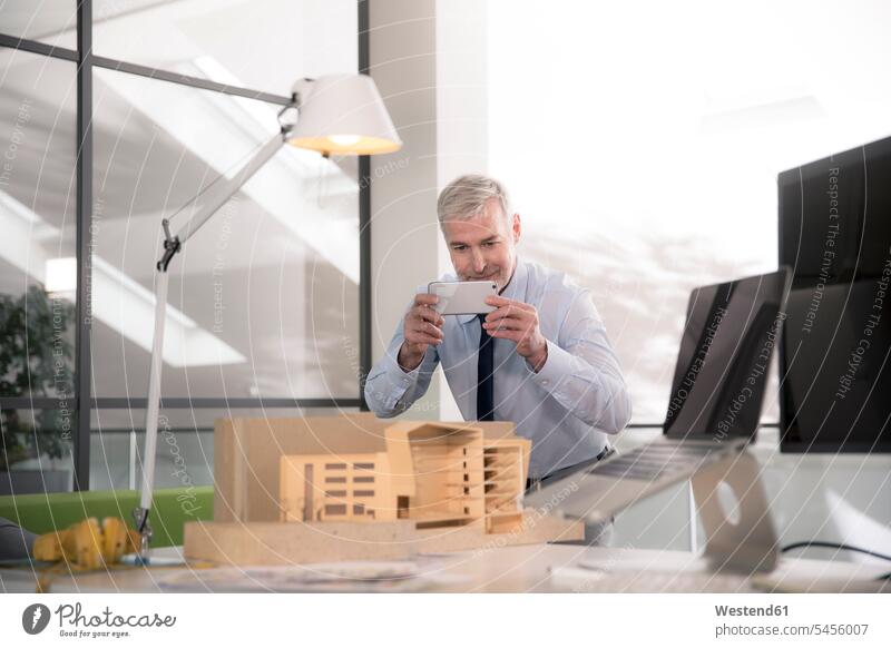 Geschäftsmann beim Fotografieren eines Architekturmodells sitzen sitzend sitzt Planungsbüro Smartphone iPhone Smartphones arbeiten Arbeit Kompetenz kompetent