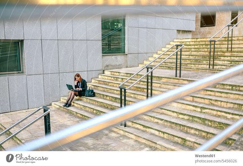 Geschäftsfrau, die auf einer Treppe sitzt und einen Laptop benutzt sitzen sitzend arbeiten Arbeit Geschäftsfrauen Businesswomen Businessfrauen Businesswoman