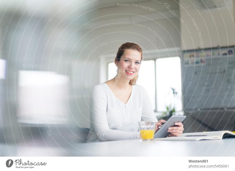 Geschäftsfrau, die in ihrem Büro am Schreibtisch arbeitet und ein digitales Tablett benutzt sitzen sitzend sitzt glücklich Glück glücklich sein glücklichsein