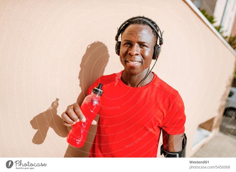 Porträt eines Mannes mit isotonischem Getränk in Sportkleidung beim Musikhören mit Kopfhörern Männer männlich Portrait Porträts Portraits Kopfhoerer Erwachsener