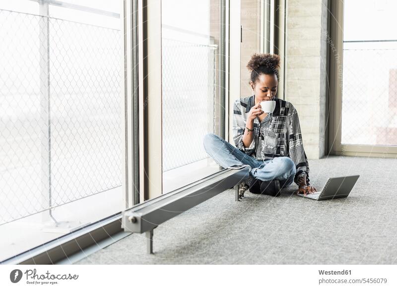 Junge Frau sitzt mit Laptop auf dem Boden und trinkt Kaffee arbeiten Arbeit Büro Office Büros Zuversicht Zuversichtlich Selbstvertrauen selbstbewusst Vertrauen