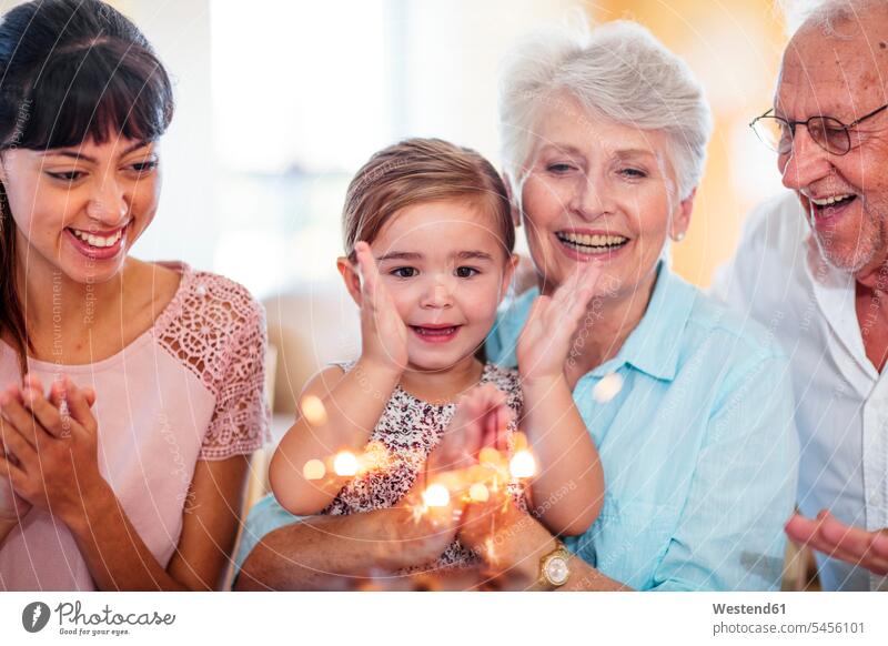 Kleines Mädchen schaut Wunderkerzen auf einem Geburtstagskuchen an und sitzt auf dem Schoß der Großmutter Wunsch Wünsche Wuensche wuenschen wünschen Enkelin