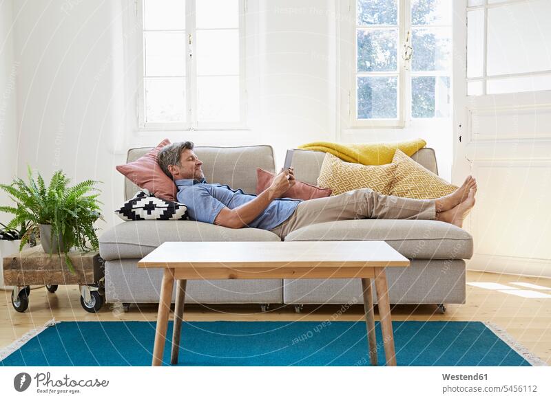 Mann liegt zu Hause auf dem Sofa und benutzt ein digitales Tablett Online Websurfen Im Net surfen Surfen bequem Zuhause daheim Männer männlich Entspannung