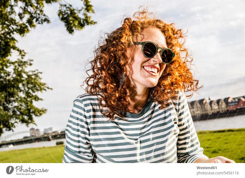 Deutschland, Köln, Porträt einer lachenden rothaarigen jungen Frau mit Sonnenbrille Portrait Porträts Portraits weiblich Frauen Erwachsener erwachsen Mensch