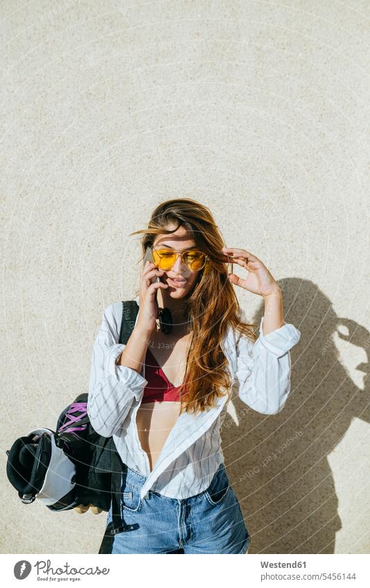 Junge Frau mit Inline-Skates in der Tasche beim Telefonieren mit dem Handy Mobiltelefon Handies Handys Mobiltelefone telefonieren anrufen Anruf telephonieren