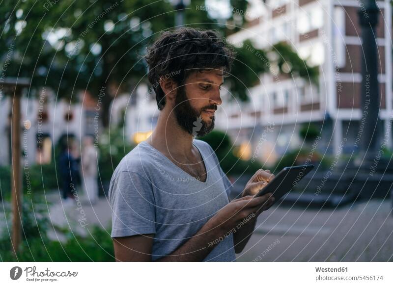 Mann betrachtet Phablet in der Stadt in der Dämmerung staedtisch städtisch Handy Mobiltelefon Handies Handys Mobiltelefone Abenddämmerung stimmungsvoll Stimmung