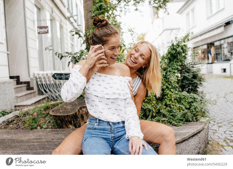 Zwei glückliche junge Frauen mit Handy in der Stadt Mobiltelefon Handies Handys Mobiltelefone Glück glücklich sein glücklichsein staedtisch städtisch weiblich