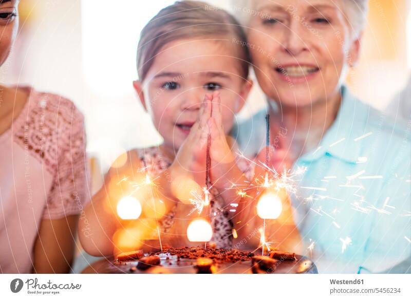 Kleines Mädchen schaut Wunderkerzen auf einem Geburtstagskuchen an und sitzt auf dem Schoß der Großmutter Geburtstagstorten Geburtstagsfeiern Geburtstage Wunsch