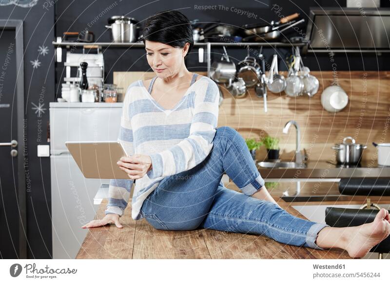 Frau sitzt am Tisch in der Küche und schaut auf die Tafel Tablet Tablet Computer Tablet-PC Tablet PC iPad Tablet-Computer weiblich Frauen Rechner Erwachsener