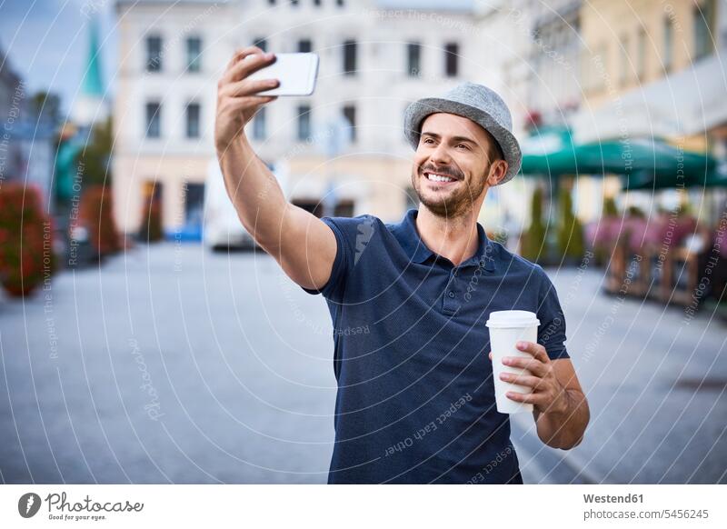 Mann macht Selfie in der Stadt mit Kaffee und Filzhut Selfies Handy Mobiltelefon Handies Handys Mobiltelefone lächeln Männer männlich glücklich Glück