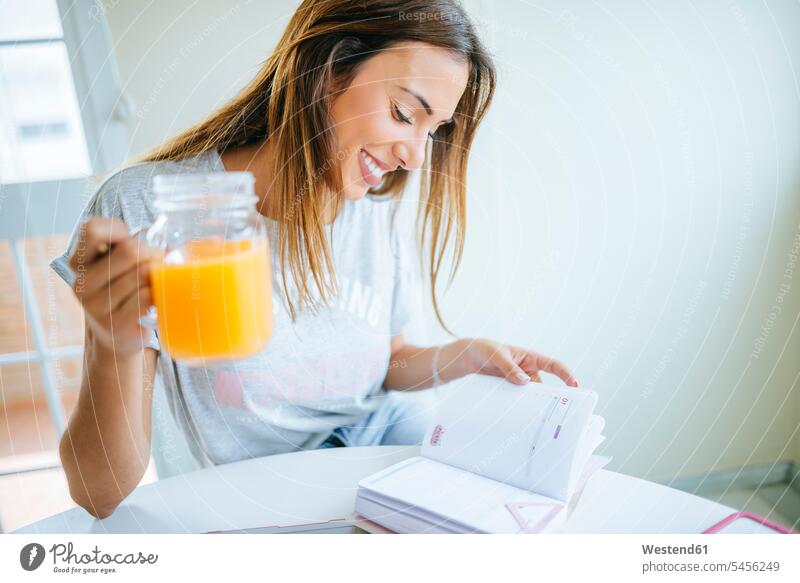 Lächelnde junge Frau mit einem Glas Orangensaft beim Blick auf die Tagesordnung weiblich Frauen Home Office homeoffice zuhause zuhause arbeiten