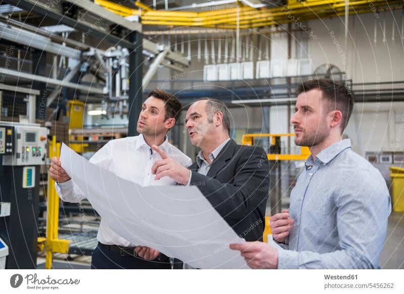 Drei Männer mit Blaupause im Gespräch in der Fabrikhalle Fabriken Mann männlich sprechen reden Kollegen Arbeitskollegen arbeiten Erwachsener erwachsen Mensch