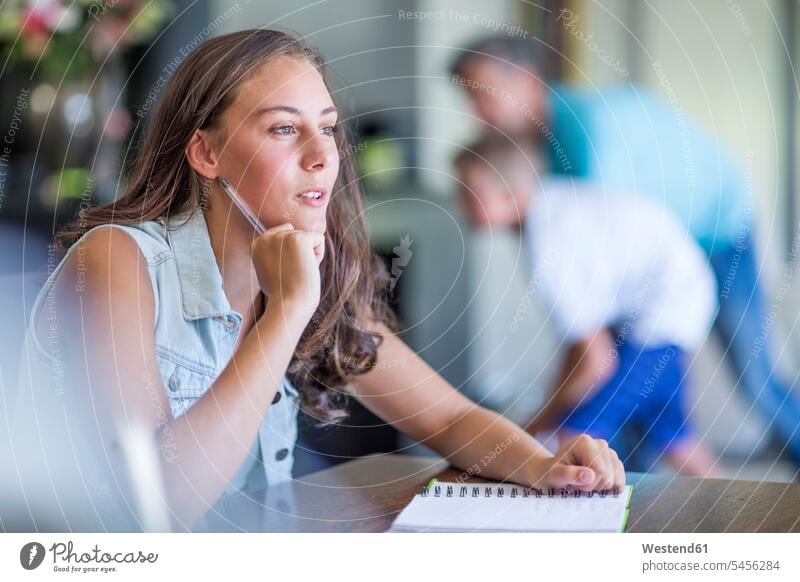 Mädchen mit Stift und Notizbuch beim Denken Hausaufgaben denken schreiben Kind Mensch Zuhause Schülerin Tisch Europäer Europäerin Tag lernen Freizeitkleidung