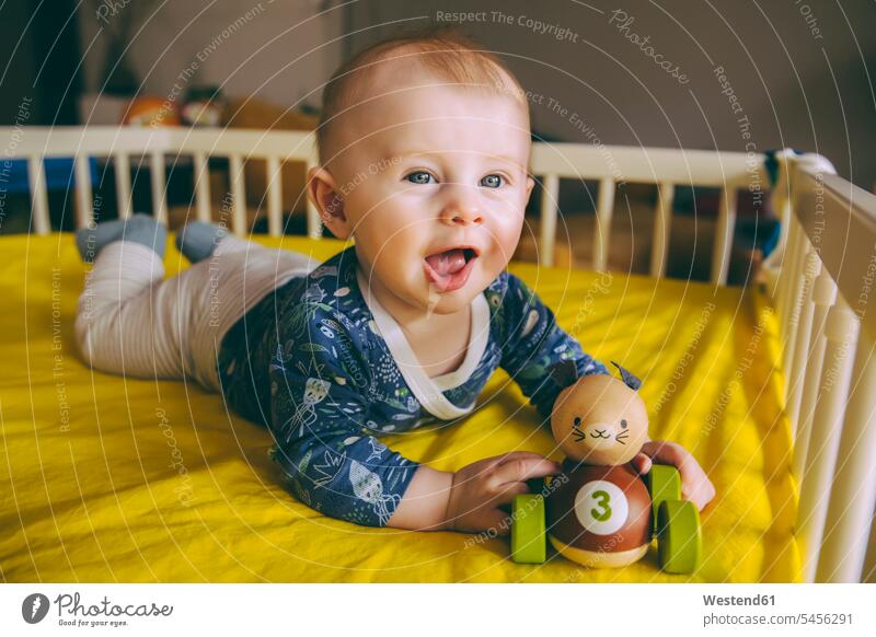 Porträt eines kleinen Jungen mit Holzspielzeug in der Krippe liegend Kinderbett Kinderbetten Portrait Porträts Portraits männliche Babys männliches Baby