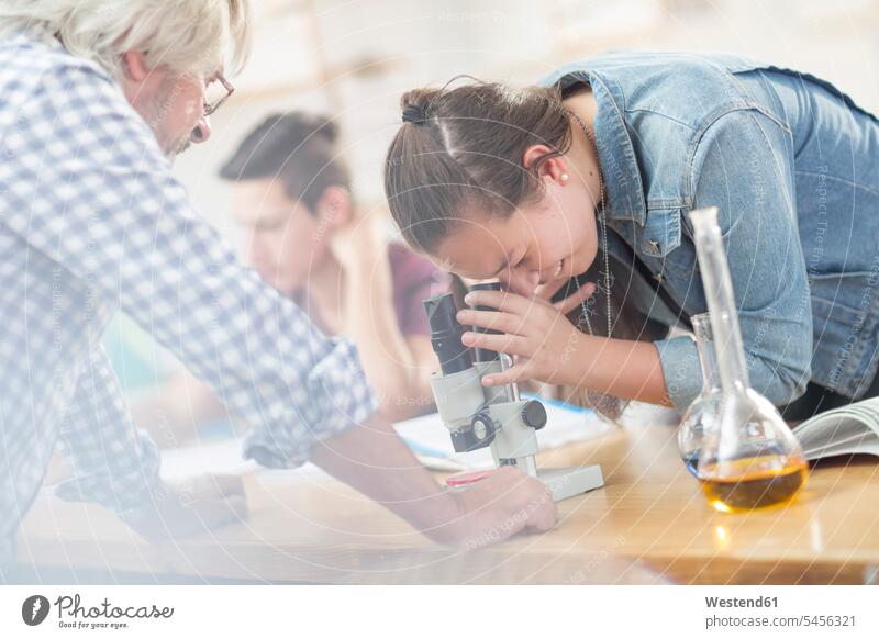 Student der Naturwissenschaften mit Lehrer in der Klasse beim Blick durchs Mikroskop Schülerin Schuelerin Schülerinnen Schuelerinnen Mikroskope lernen Bildung